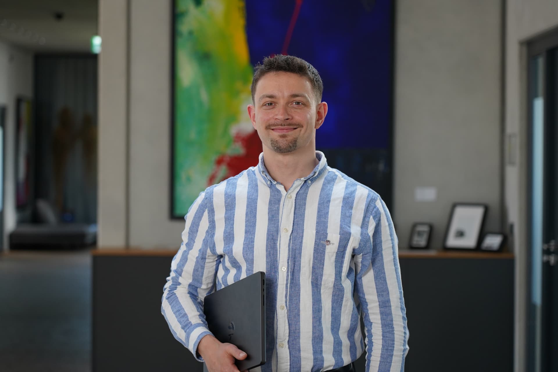 T4D-Berater mit Laptop im Büro, freundlich in die Kamera blickend